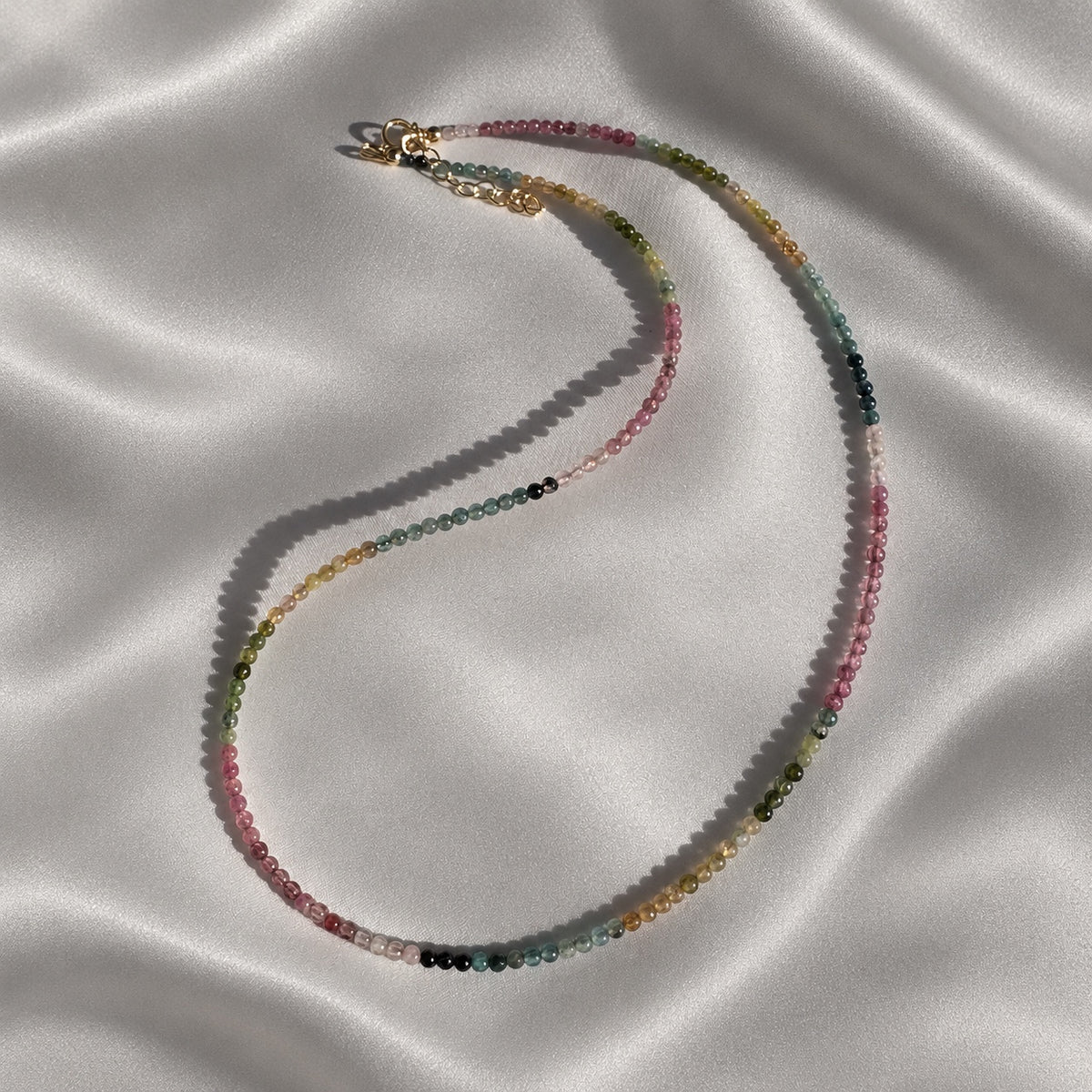 Full COLOUR POEM necklace showing its fine line of smooth 2 mm tourmaline beads and 14k gold-filled details on pearl-grey silk